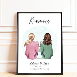 May include: A framed print featuring a digital illustration of two people sitting side-by-side, seen from behind. The text reads Roomies, Claire & Lisa, EST. 2023, and home away from home. One person has blonde hair and a pink sweater, the other brown hair and a green sweater.