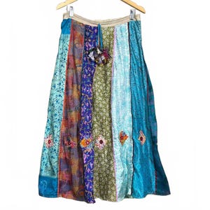 May include: A long, multi-paneled skirt featuring a vibrant patchwork of various fabrics in shades of blue, green, orange, and purple. The skirt includes intricate floral and geometric patterns, decorative embroidered diamond accents, and a fabric tassel.