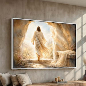 May include: A framed canvas print depicts a figure in flowing white robes exiting a stone tomb into bright light. The artwork features soft, warm tones and a serene, spiritual theme. The print is displayed above a wooden bench with pillows.