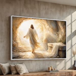 May include: A framed canvas print depicts a figure in flowing white robes emerging from a stone tomb, bathed in golden light. The artwork features a serene, spiritual theme, with a focus on light and shadow.