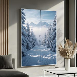 May include: A framed print of a snowy ski slope scene. The image features a ski lift ascending between snow-covered evergreen trees. Mountains are visible in the background, with a bright blue sky and a touch of fog.