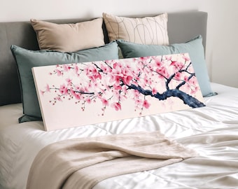 May include: A rectangular canvas print featuring a watercolor painting of a cherry blossom branch with pink flowers and a dark blue branch. The artwork is displayed on a bed with pillows and a blanket.