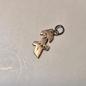 May include: A silver pendant with a cross design and a small loop. The pendant has a textured surface and a unique shape, possibly representing a religious symbol or a decorative element. The pendant is made of silver.
