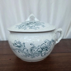 Puede incluir: Una taza de cerámica blanca con asa negra y el texto "But First, Coffee" en negrita negra. La taza se encuentra sobre una superficie blanca, mostrando su diseño limpio.