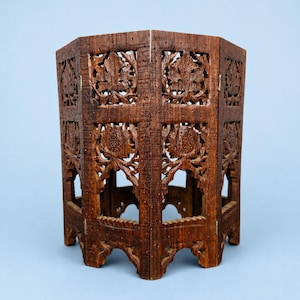 May include: A dark brown, intricately carved wooden side table. The table features floral and leaf patterns, with openwork designs. The table has a hexagonal shape and is made of wood. The table is approximately 18 inches tall.