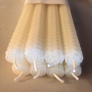 May include: A bundle of 10 white beeswax candles, hand rolled and arranged in a honeycomb pattern. The candles are wrapped in white paper with the text "HAND ROLLED BEE WAX CANDLES".