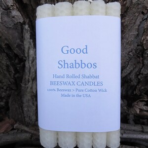 May include: A package of white beeswax candles with a label that reads "Good Shabbos", "Hand Rolled Shabbat Beeswax Candles", "100% Beeswax > Pure Cotton Wick", and "Made in the USA".