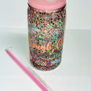 May include: A clear tumbler filled with colorful glitter and the text "I can do all things through Christ who strengthens me" in copper. The tumbler has a pink lid and comes with a pink straw.