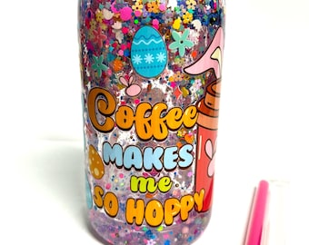 May include: A clear plastic tumbler with a red lid filled with colorful glitter and confetti. The tumbler has a graphic that says "Coffee makes me so hoppy" with Easter-themed illustrations. A pink straw is next to the tumbler.