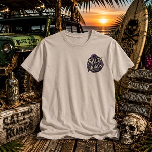 May include: A cream-colored short-sleeve t-shirt featuring a circular graphic on the left chest. The graphic displays a purple octopus wrapped around the text Salty Roads in a stylized font. The shirt has a crew neckline and a standard fit.