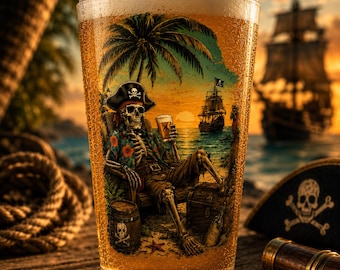 May include: A clear glass pint filled with golden beer featuring a printed graphic of a skeleton wearing a pirate hat and a floral shirt, sitting in a chair on a beach with a drink, a treasure chest, a barrel, and a sailing ship in the background.
