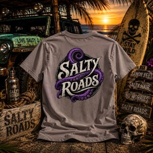 May include: A grey short-sleeve t-shirt featuring a graphic on the back of a purple octopus tentacle wrapped around a black circle with the white text Salty Roads. The design is centered on the fabric, showcasing a bold, illustrative style.