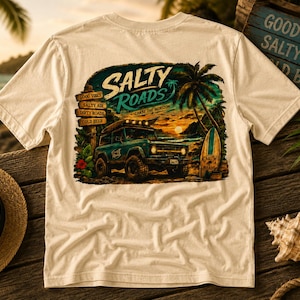 May include: A cream-colored t-shirt featuring a graphic print on the back. The design depicts a teal off-road vehicle on a beach at sunset, a surfboard, a palm tree, and a signpost with the text Salty Vibes, Salty Air, Dirty Roads, Cold Beer.