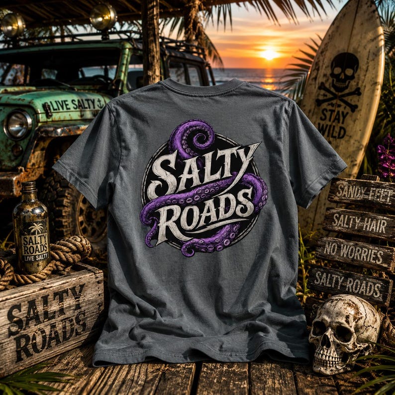 May include: A charcoal gray short-sleeve t-shirt featuring a circular graphic on the back. The design includes a purple octopus tentacle wrapped around the white text Salty Roads. The shirt is displayed against a beach-themed background.