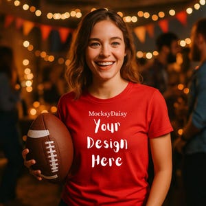 Könnte beinhalten: Ein rotes T-Shirt mit dem weißen Text "Your Design Here". Eine Person hält einen braunen und weißen Football. Der Hintergrund ist verschwommen mit warmen Lichtern. Das T-Shirt hat einen Rundhalsausschnitt.
