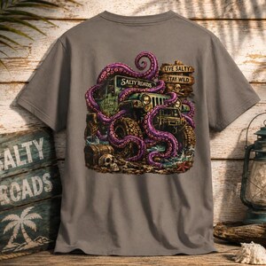 May include: A grey t-shirt featuring a graphic of a purple octopus wrapped around an off-road vehicle. The design includes a wooden sign with the text "LIVE SALTY STAY WILD" and "SALTY ROADS," a skull, a treasure chest, and a starfish on the ground.