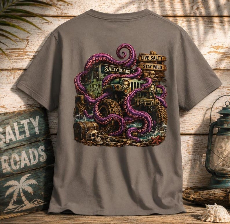 May include: A grey t-shirt featuring a graphic of a purple octopus wrapped around an off-road vehicle. The design includes a wooden sign with the text "LIVE SALTY STAY WILD" and "SALTY ROADS," a skull, a treasure chest, and a starfish on the ground.