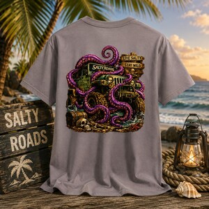 May include: A grey t-shirt featuring a graphic of a green off-road vehicle wrapped in purple octopus tentacles. The design includes a wooden sign with the text "LIVE SALTY STAY WILD" and "SALTY ROADS," a skull, and a treasure chest.