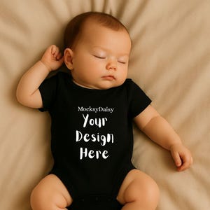 Könnte beinhalten: Ein schlafendes Baby in einem schwarzen Body. Auf dem Body steht in Weiß der Text "MocksyDaisy Your Design Here". Das Baby liegt auf einer beigen Oberfläche.