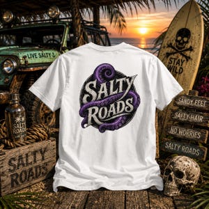May include: A white t-shirt featuring a circular graphic on the back with the text Salty Roads in a stylized font, wrapped by a purple octopus tentacle. The design is centered on the fabric, showcasing detailed suction cups and shading.