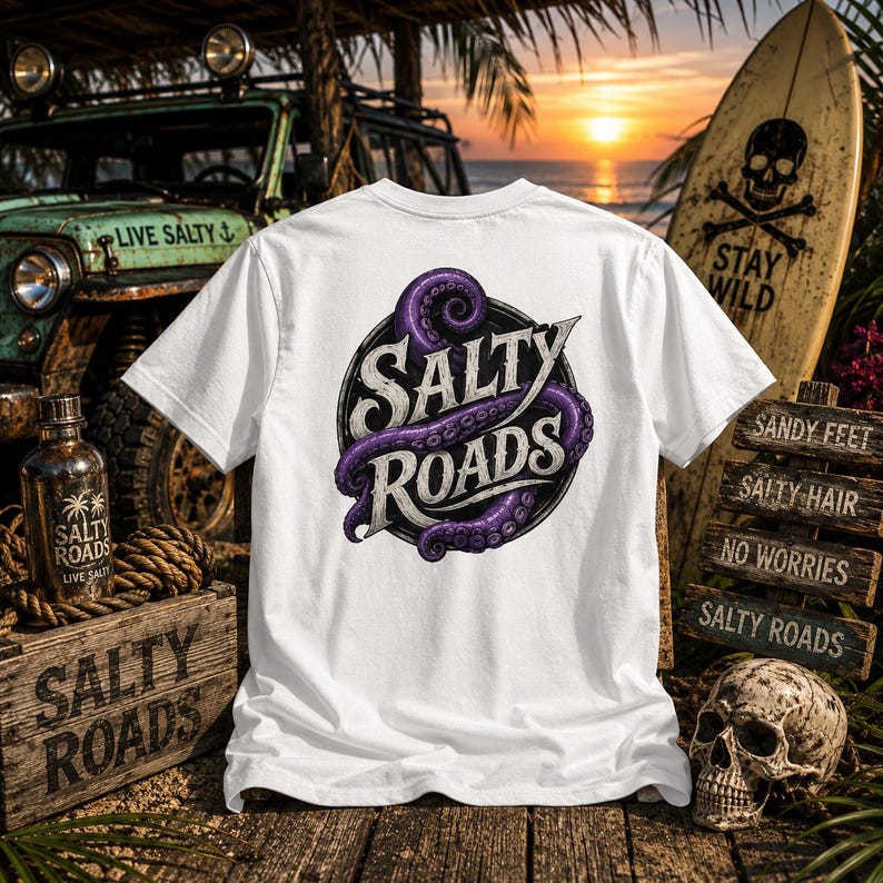 May include: A white t-shirt featuring a circular graphic on the back with the text Salty Roads in a stylized font, wrapped by a purple octopus tentacle. The design is centered on the fabric, showcasing detailed suction cups and shading.