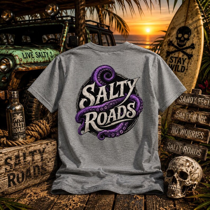 May include: A heather gray short-sleeve t-shirt featuring a circular graphic on the back. The design includes a purple octopus tentacle wrapped around the white text SALTY ROADS. The shirt is displayed against a backdrop of a vehicle and a surfboard.