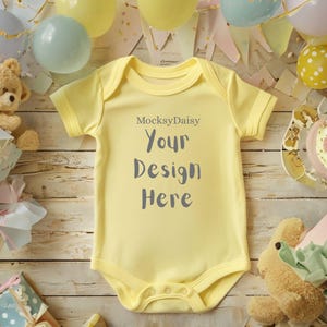 Könnte beinhalten: Ein hellgelber Baby-Body mit kurzen Ärmeln und Druckknöpfen. Der Text "MocksyDaisy Your Design Here" ist auf der Vorderseite aufgedruckt. Der Body ist von Partydekorationen umgeben, darunter Luftballons und Stofftiere.