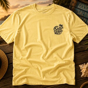 May include: A pale yellow short-sleeve t-shirt featuring a black circular graphic on the left chest. The graphic depicts a palm tree and a starfish with the text Salty Roads written in a stylized script font across the center of the circle.