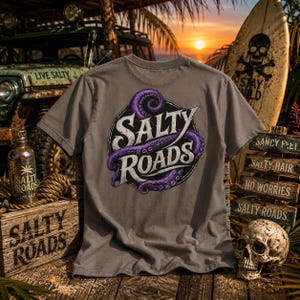 May include: A charcoal gray short-sleeve t-shirt featuring a circular graphic on the back with a purple octopus tentacle wrapped around the white text Salty Roads. The design is set against a backdrop of a vehicle, a surfboard, and a skull.