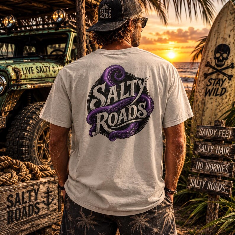 May include: A light-colored short-sleeve t-shirt featuring a circular graphic on the back with purple octopus tentacles wrapped around the text Salty Roads. The shirt is worn with dark shorts patterned with palm trees and a black baseball cap.