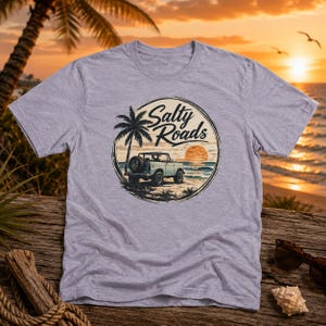 May include: A heather gray t-shirt featuring a circular graphic on the chest. The design depicts a palm tree, a vintage off-road vehicle on a beach, and a sunset over the ocean, with the text Salty Roads written in a script font.