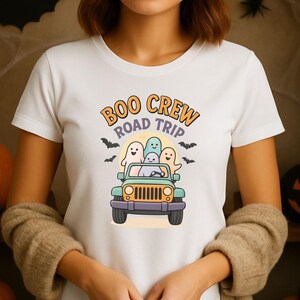 May include: White t-shirt featuring a Halloween-themed graphic. The design includes the text "Boo Crew Road Trip" above a cartoon jeep filled with ghosts and bats. The jeep is green and purple.