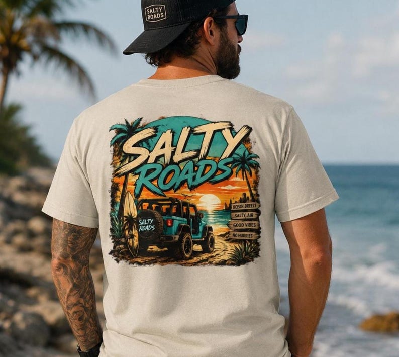 May include: A beige short-sleeve t-shirt featuring a graphic on the back of a teal off-road vehicle on a beach at sunset. The text reads SALTY ROADS, OCEAN BREEZE, SALTY AIR, GOOD VIBES, and NO HUMMIES. A surfboard is attached to the vehicle.