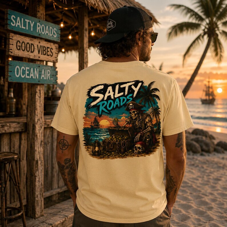 Puede incluir: Una camiseta de manga corta color crema con un gr&aacute;fico en la espalda. El dise&ntilde;o muestra un esqueleto pirata con un cofre del tesoro, un farol y un barco al atardecer. El texto "SALTY ROADS" est&aacute; impreso en una fuente llamativa sobre la escena.