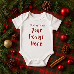 Könnte beinhalten: Ein weißer Baby-Body mit dem roten Text "MocksyDaisy Your Design Here". Das Bild ist vor einem festlichen Hintergrund mit Weihnachtsdekorationen, darunter Tannennadeln, rote Kugeln, Tannenzapfen und Zimtstangen.