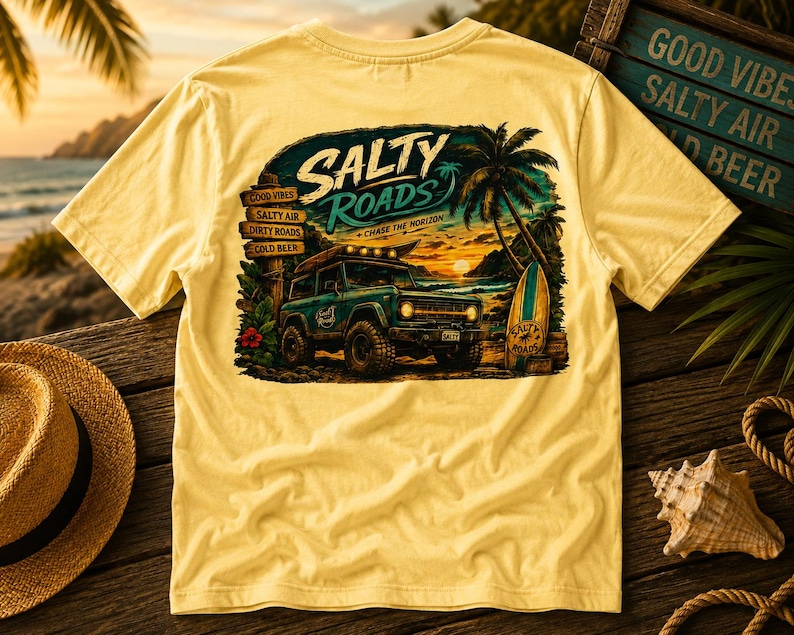 May include: A pale yellow t-shirt featuring a graphic on the back of a teal off-road vehicle parked on a beach at sunset. The design includes palm trees, a surfboard, and text that reads Salty Roads, Chase the Horizon, and Good Vibes.