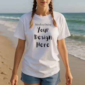 Könnte beinhalten: Weißes T-Shirt mit dem Text "MocksyDaisy Your Design Here" in Schwarz. Das T-Shirt wird an einem Strand getragen. Das Model trägt blaue Jeansshorts.