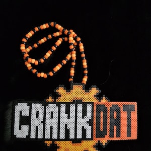 May include: A beaded necklace with the word "CRANKDAT" spelled out in white and orange beads. The necklace has a black background and the beads are orange and black.