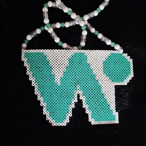 May include: A beaded pendant featuring the letters "WP" in turquoise and white. The pendant is made of small, round beads and is connected to a necklace of white and green beads. The background is black.
