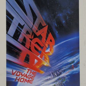 May include: A vintage movie poster for the film "Star Trek: The Voyage Home". The poster features a red and blue image of the Starship Enterprise flying towards Earth, with the text "Beaming Down to Earth December 12, 1986." and "The Voyage Home" in the bottom left corner.