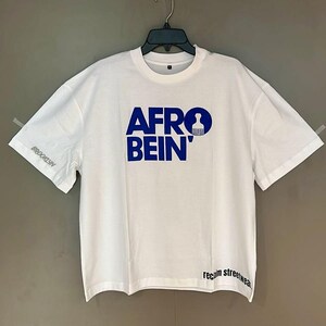 May include: White t-shirt with the blue text "AFRO BEIN'" and a graphic. The sleeve has "BROOKLYN" printed in gray. The bottom of the shirt has the text "reclaim streetwear."