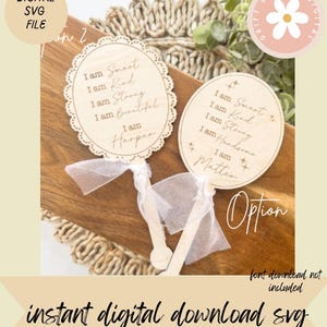 May include: Two wooden signs with the phrases "I am Smart, Kind, Strong, Beautiful" and "I am Smart, Kind, Strong, Handsome". Each sign has a name at the bottom and is attached to a wooden stick with a white ribbon. The signs are on a wooden surface.