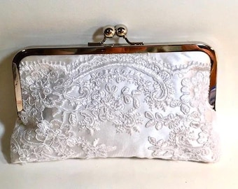 May include: A white satin clutch purse with a silver metal frame and a delicate lace design.