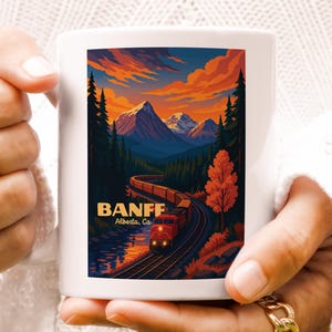May include: White ceramic mug featuring a colorful illustration of a train traveling through a mountain landscape at sunset. The design includes the text "BANFF Alberta, CA."