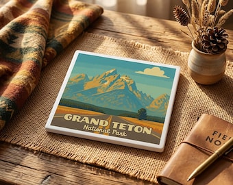 May include: A square ceramic coaster featuring a graphic illustration of the Grand Teton National Park with snow-capped mountains, a road, and a blue sky. The text reads GRAND TETON National Park in a bold, sans-serif font.