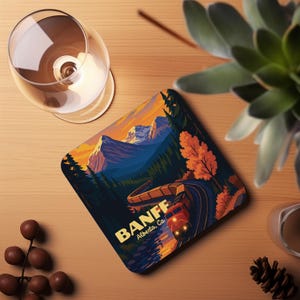 May include: Square coaster featuring a scenic illustration of Banff, Alberta, with a train winding through a mountain landscape. The design includes a sunset with orange, yellow, and blue hues. The coaster has the text "BANFF Alberta, Ca."