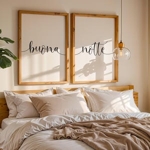 Op de afbeelding: Twee ingelijste kunstdrukken met de woorden "buona" en "notte" in cursief schrift. De prints zitten in houten frames en hangen boven een bed met wit beddengoed en een bruine deken. Een moderne slaapkamer.