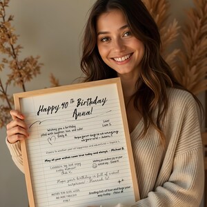 May include: A framed sign with the message "Happy 40th Birthday Anna!" in black script, filled with birthday wishes and signatures. The woman holding the sign is smiling. The frame is made of wood.
