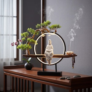 May include: A decorative zen garden display featuring a white ceramic Buddha statue, a small bonsai tree, and a glowing circular light. Incense smoke rises from a lotus flower. The display sits on a dark wooden table.