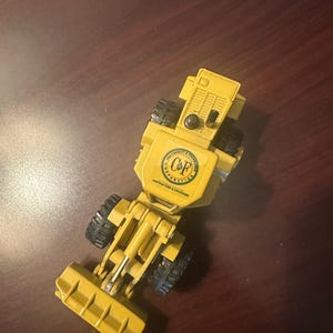 May include: A yellow toy construction vehicle featuring a front loader bucket, black rubber tyres, and a circular logo on the top hood that reads C&F Corporation, The Conduit & Foundation Corporation, Contractors & Engineers in black text.